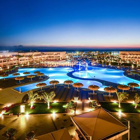 Hotel Pickalbatros Royal Moderna Sharm "Aqua Park" Esterno foto The photo showcases an elegant resort area at dusk. It features a large swimming pool, which is beautifully illuminated with blue lights, creating a serene and inviting atmosphere. Surrounding the pool are palm trees and umbrellas, enhancing the trop