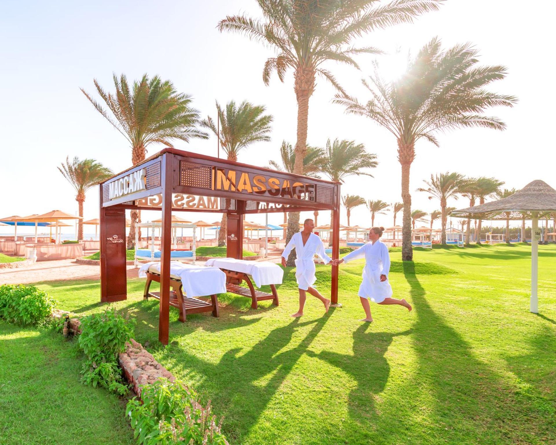 Hotel Pickalbatros Royal Moderna Sharm "Aqua Park" Esterno foto The photo shows a serene outdoor spa area, featuring a massage pavilion with a sign that reads "MASAGE." There are two individuals in white robes, appearing to enjoy a light-hearted moment while walking towards the pavilion. Surrounding the pavilion 