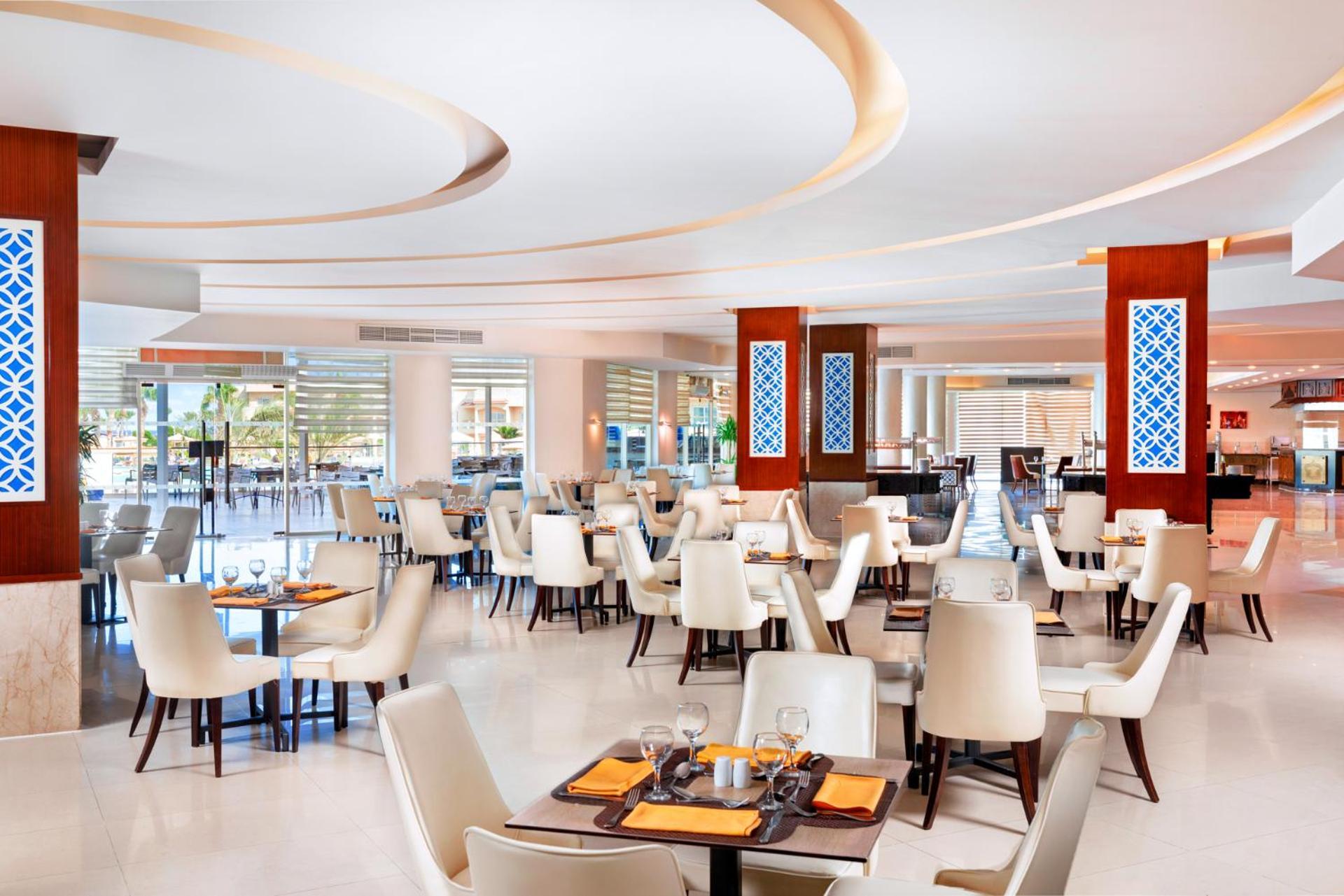 Hotel Pickalbatros Royal Moderna Sharm "Aqua Park" Esterno foto The photo shows a modern restaurant interior. The design features light, neutral colors with elegant white chairs and wooden tables. The layout includes several dining tables set for customers, creating a spacious and inviting atmosphere. There are d