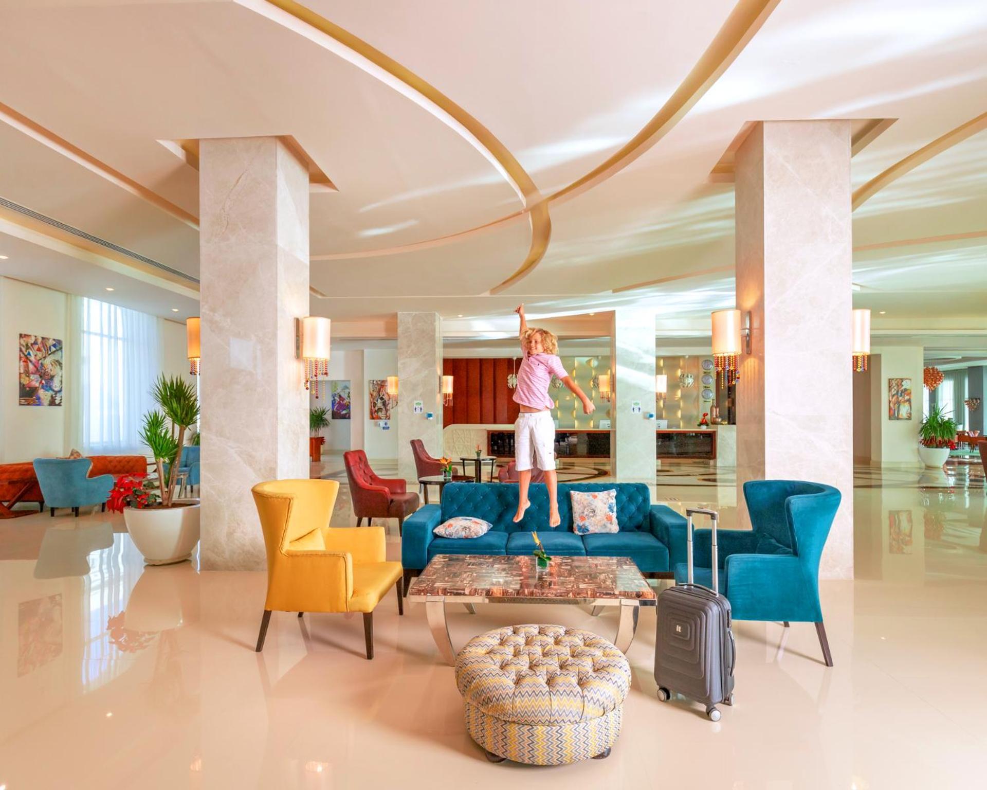 Hotel Pickalbatros Royal Moderna Sharm "Aqua Park" Esterno foto The photo shows a modern and stylish hotel lobby. There's a spacious area with elegant decor, featuring large pillars and contemporary lighting. A colorful arrangement of furniture includes teal, yellow, and red chairs. A person is standing on a larg